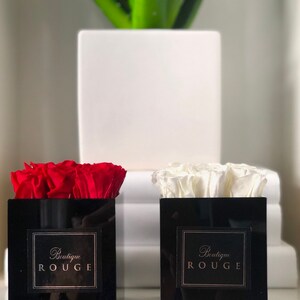 May include: Two black square boxes with red and white roses inside. The boxes have a gold label that says "Boutique Rouge".
