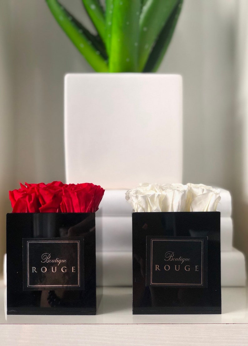 May include: Two black square boxes with red and white roses inside. The boxes have a gold label that says "Boutique Rouge".
