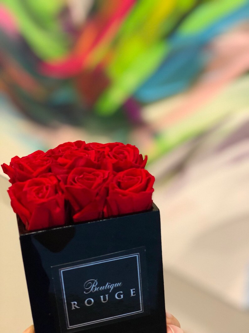 May include: A black square box with a red rose arrangement. The box has a white label with the text "Boutique Rouge".