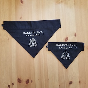 Könnte beinhalten: Zwei schwarze Stoffbandanas mit weiß gesticktem Text und einem Symbol. Die größere Bandana trägt den Schriftzug "Malevolent Familiar" und die kleinere Bandana trägt denselben Schriftzug. Beide Bandanas zeigen ein weißes Symbol eines Kreuzes mit einem Unendlichkeitszeichen.