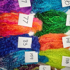 May include: A collection of colorful, textured yarn in various shades, including purple, blue, green, orange, and yellow. Each bundle is labeled with a number on a white tag. The yarn appears to be a specialty fiber, possibly for knitting or other crafts.