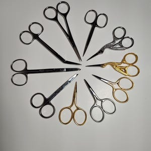 Puede incluir: Una variedad de tijeras de diferentes estilos y tamaños, dispuestas en un patrón circular. Las tijeras presentan tonos plateados y dorados, algunas con mangos decorativos. Las hojas son afiladas y puntiagudas, lo que sugiere su uso en manualidades o aseo.