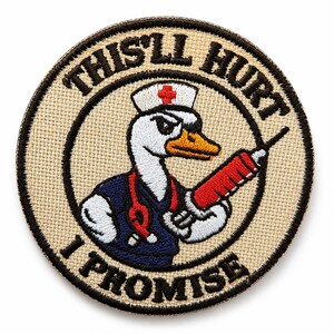 May include: Circular patch featuring a cartoon goose in a nurse's uniform, holding a red syringe. The text "THIS'LL HURT I PROMISE" is displayed in black. The patch has a tan background and a black border.