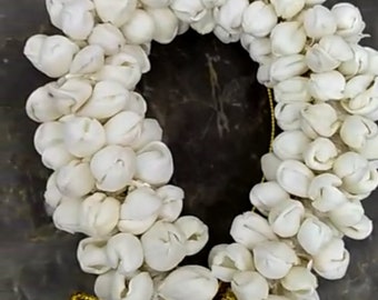 Può includere: Un accessorio per capelli floreale circolare, con numerosi boccioli di fiori bianchi disposti ad anello. I fiori sono raggruppati, creando un aspetto denso e strutturato. Un nastro color oro è legato alla base dell'anello.