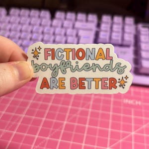 May include: A sticker with the text "Fictional boyfriends are better" in rainbow colors with stars on either side.