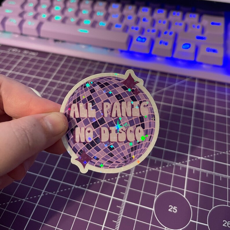 以下が含まれることがあります： レトロなフォントで「ALL PANIC NO DISCO」と書かれた、ディスコボールのデザインのホログラフィックステッカーです。