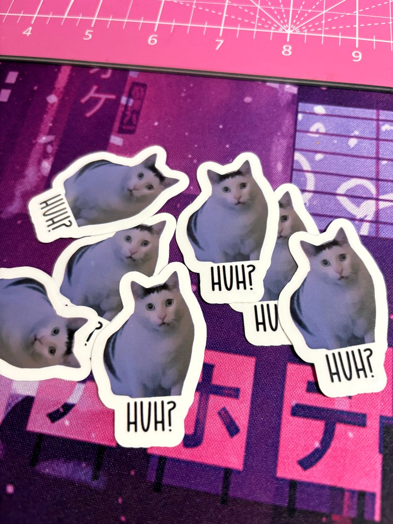 May include: Six white and gray cat stickers with the text "HUH?" on each. The stickers are on a purple and pink background.