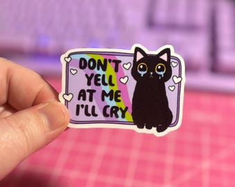 May include: A black cat sticker with a rainbow background and the text "Don't yell at me I'll cry". The cat has tear drops coming from its eyes and there are hearts around the cat.