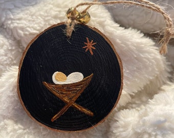Peut inclure: Une décoration de Noël en bois peinte en noir avec une crèche dorée et deux œufs blancs à l'intérieur. Une étoile dorée est peinte sur le dessus de l'ornement.