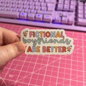 May include: A sticker with the text "Fictional boyfriends are better" in rainbow colors with glitter accents.