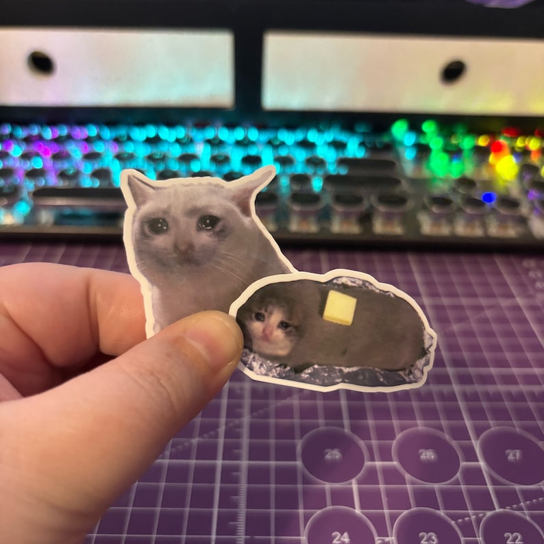 May include: Two stickers featuring the crying cat meme. One sticker shows a gray cat with a sad expression. The other sticker depicts a cat inside a baked potato with a pat of butter.