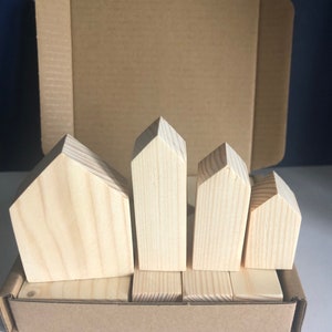 May include: A set of five wooden houses in various sizes, arranged in a row in a cardboard box. The houses are made of unfinished light brown wood.