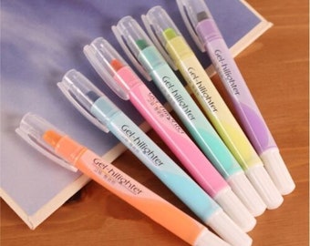 Könnte beinhalten: Sechs pastellfarbene Gel-Textmarker mit durchsichtigen Kunststoffgehäusen und weißen Kappen. Die Textmarker sind mit "Gel-hilighter" in schwarzer Schrift beschriftet.