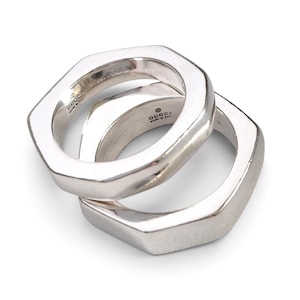 May include: Two interlocking silver rings with a polished finish and an octagonal shape. The interior of each band is engraved with the Gucci logo and the text Made in Italy, along with a 925 hallmark indicating sterling silver composition.