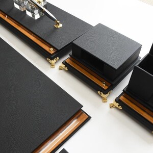 May include: Black leather desk organizer set with gold accents. The set includes a pen holder, a letter holder, and a multi-compartment organizer.