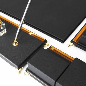 May include: Black leather desk organizer set with gold accents. The set includes a pen holder, two inkwells, and a writing surface.