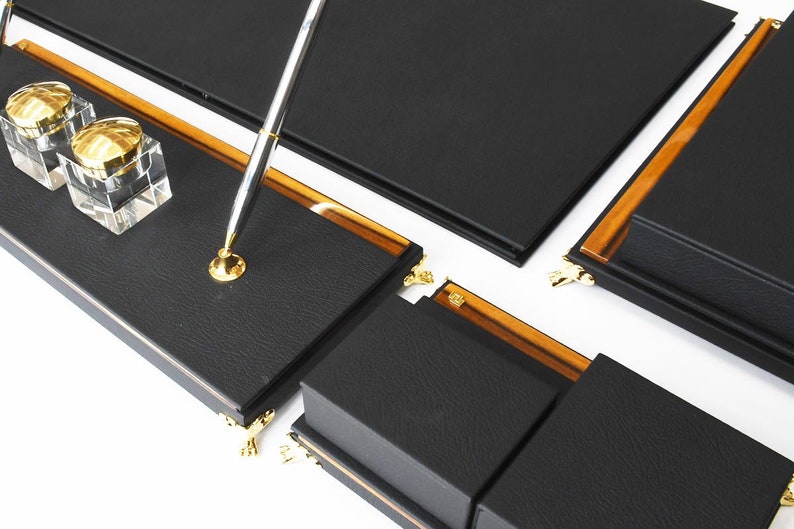 May include: Black leather desk organizer set with gold accents. The set includes a pen holder, two inkwells, and a writing surface.