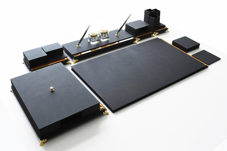 May include: Black leather desk organizer set with gold accents. The set includes a large writing surface, a smaller writing surface, a pen holder, a notepad holder, and a set of coasters.