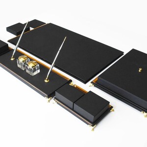 May include: Black leather desk organizer set with gold accents. The set includes a writing pad, pen holders, and a tray for office supplies.