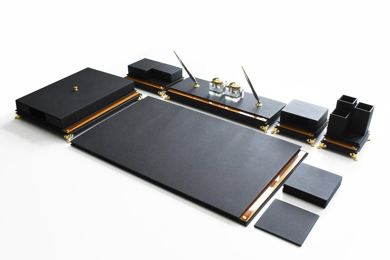 May include: Black leather desk organizer set with gold accents. The set includes a large writing pad, a pen holder, two inkwells, a letter tray, and a small tray.