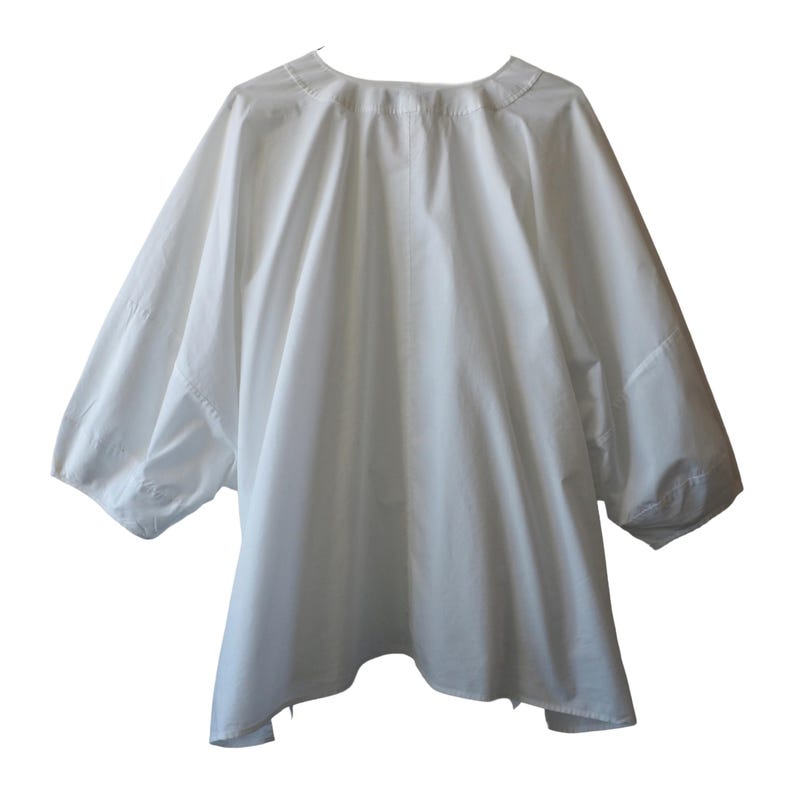 May include: A white, loose-fitting top with three-quarter sleeves. The garment has a rounded neckline and a flowing, oversized silhouette. The fabric appears to be a lightweight material, suitable for warmer weather. The sleeves are gathered at the elbow.
