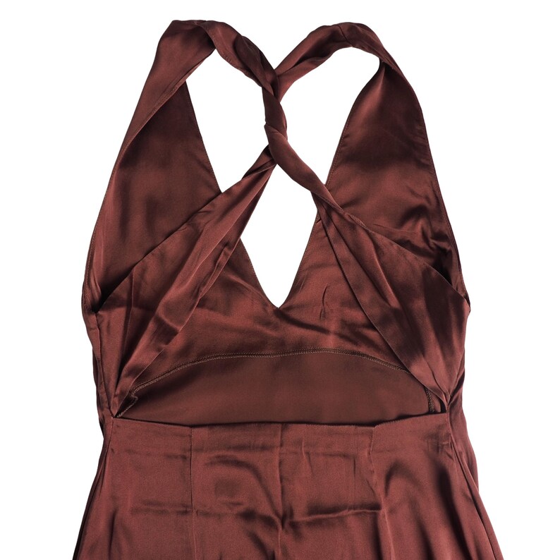 May include: A dark brown satin dress featuring a deep V-neckline and a distinctive twisted halter strap design that crosses at the back. The garment has a smooth, lustrous finish and a sleeveless cut, showcasing a clean, minimalist construction.
