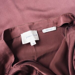 May include: A dark mauve garment with a smooth, satin-like finish. The interior features a white fabric label with the text 'paloma wool' in blue, a smaller tag below it with the number '36', and a separate tag reading 'Made in Spain'.