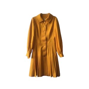 May include: A long-sleeved, yellow dress with a collared neckline and button closure. The dress has a pleated skirt and long sleeves with button cuffs.