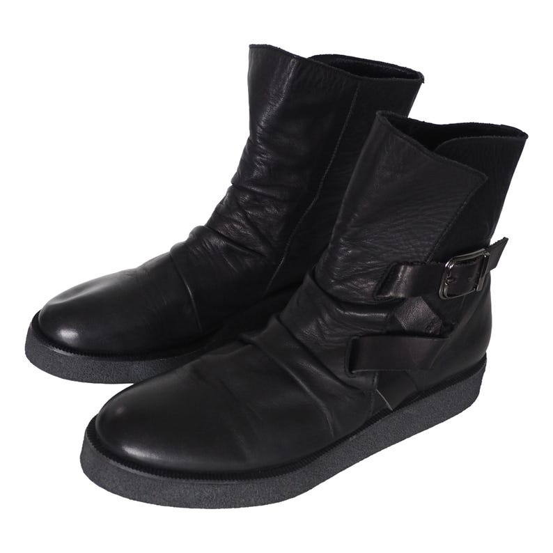 May include: A pair of black ankle boots featuring a smooth leather upper with subtle ruching, a rounded toe, and a side strap with a dark metal buckle. The boots are set on a thick, textured dark gray rubber sole with a flat profile and low heel.