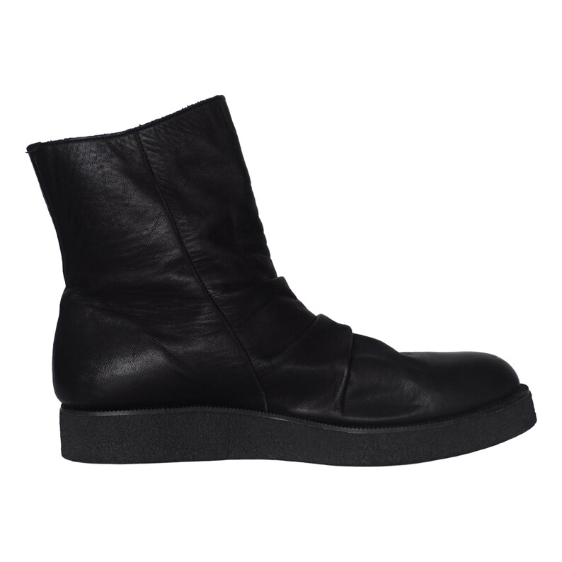 May include: A black leather ankle boot featuring a smooth upper with subtle gathered detailing across the midfoot, a rounded toe, and a thick, textured black rubber platform sole that provides a flat base for the footwear.