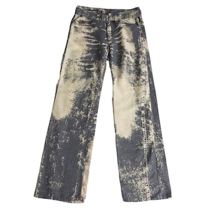 May include: A pair of wide-leg jeans with a unique distressed design. The denim is primarily dark gray with lighter beige patches, creating a textured, worn appearance. The jeans have a classic five-pocket design and a button and zipper closure.