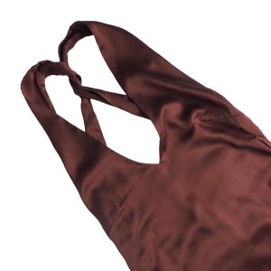 May include: A dark brown sleeveless top with a smooth, satin-like finish. The garment features a deep V-neckline and wide shoulder straps that cross over each other at the upper back, creating a distinct twisted detail in the fabric construction.