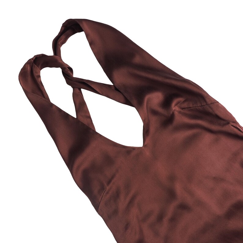 May include: A dark brown sleeveless top with a smooth, satin-like finish. The garment features a deep V-neckline and wide shoulder straps that cross over each other at the upper back, creating a distinct twisted detail in the fabric construction.