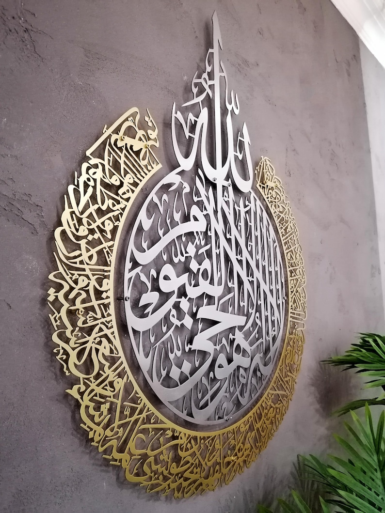 Op de afbeelding: Een groot, cirkelvormig wandkunstwerk met ingewikkelde Arabische kalligrafie. Het ontwerp bestaat uit een zilverkleurig middengedeelte omringd door een goudkleurige buitenrand, beide met gedetailleerde, lasergesneden schriftpatronen.