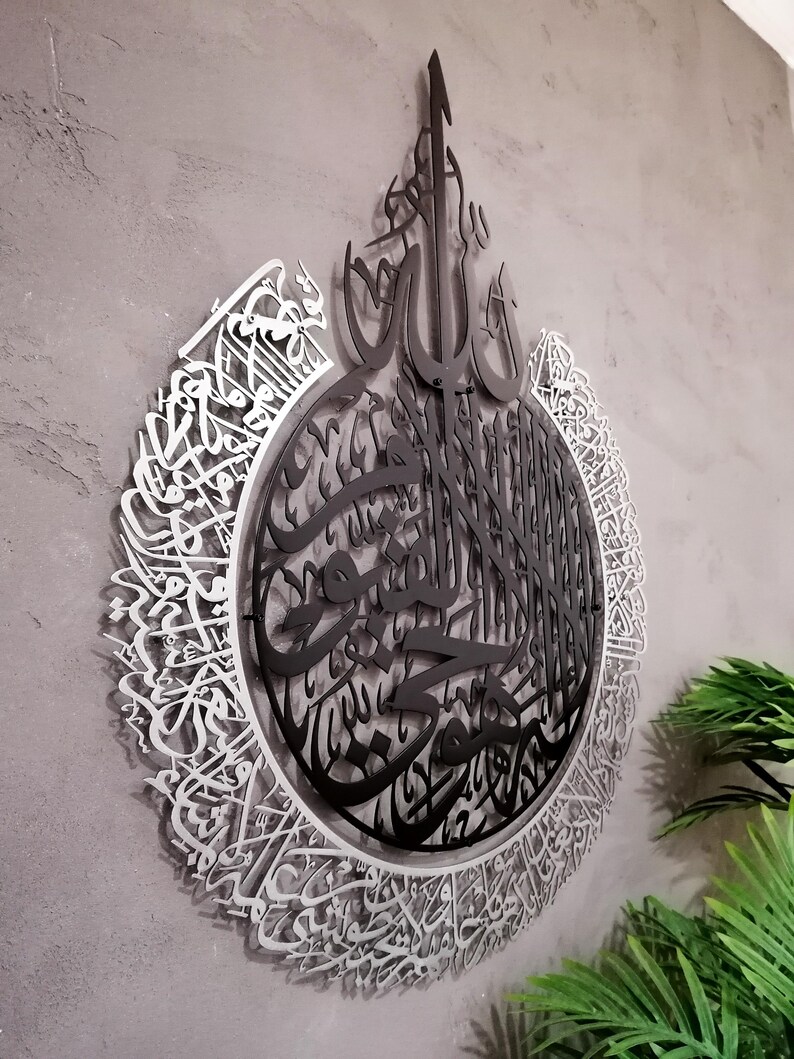 Op de afbeelding: Een cirkelvormig wandkunstobject met complexe Arabische kalligrafie. Het ontwerp bestaat uit een zwart middengedeelte met gedetailleerd schrift, omringd door een zilverkleurige buitenring van sierlijke, vloeiende Arabische letters.