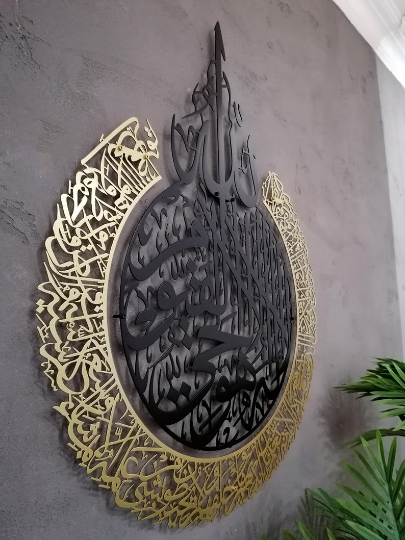 Op de afbeelding: Een cirkelvormig wandkunstobject met ingewikkelde Arabische kalligrafie. Het ontwerp bestaat uit een centrale zwarte metalen laag met gedetailleerd schrift, omringd door een grotere goudkleurige metalen rand met uitgebreide kalligrafische patronen.