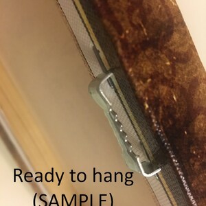 May include: Close-up of a brown canvas painting with a metal hanging hook attached to the back. The text "Ready to hang (SAMPLE)" is printed on the canvas.