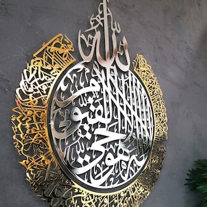Op de afbeelding: Een groot, cirkelvormig wandkunstwerk met ingewikkelde Arabische kalligrafie in een gepolijste gouden afwerking. Het ontwerp bevat een zilverkleurig middengedeelte met gedetailleerd schrift, omringd door een sierlijke, filigraan gouden rand.