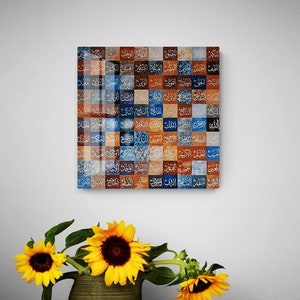 Pode incluir: Uma peça de arte de parede quadrada com um mosaico de quadrados coloridos. Cada quadrado apresenta uma palavra árabe diferente em letras brancas. O fundo dos quadrados é uma mistura de tons azuis, marrons e laranja.