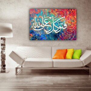 May include: A colorful abstract painting with white Arabic calligraphy. The painting is framed and hanging on a wall above a white couch with orange and yellow throw pillows.