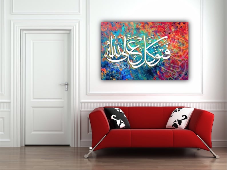 May include: A colorful abstract canvas print with white Arabic calligraphy that reads "Subhana Allahi wa bihamdihi, Subhana Allahi al-Azim". The print is hanging on a white wall above a red couch.