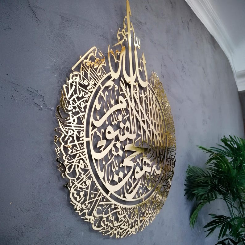 Op de afbeelding: Een groot, cirkelvormig wandkunstobject van goudkleurig metaal met ingewikkelde, lasergesneden Arabische kalligrafie. Het ontwerp is zeer gedetailleerd met sierlijke, vloeiende schriftpatronen die een samenhangend en decoratief geheel vormen.