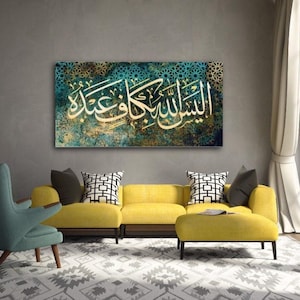 Op de afbeelding: Een groot rechthoekig canvas kunstwerk met witte Arabische kalligrafie tegen een turquoise en gouden achtergrond. Het kunstwerk hangt boven een gele bank met decoratieve kussens, wat een blikvanger creëert in een moderne woonkamer.