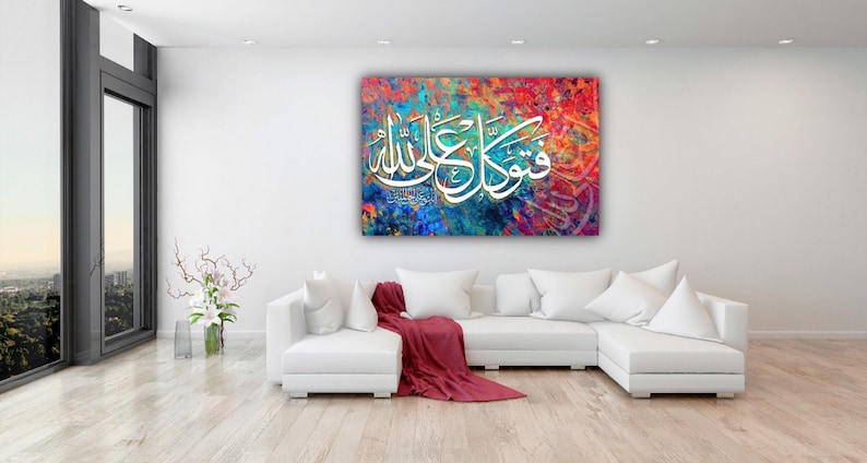 May include: A white couch with red throw blanket in front of a colorful abstract painting with Arabic calligraphy that reads "Allah" and "Muhammad".