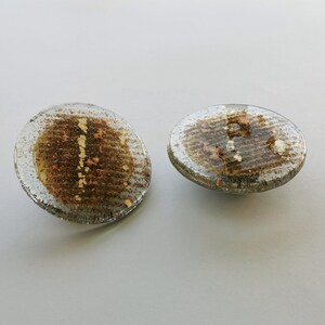 Peut inclure: Deux sous-verres ronds en verre avec un motif moucheté brun et or. Les sous-verres ont un dessus en verre transparent et un dessous argenté.