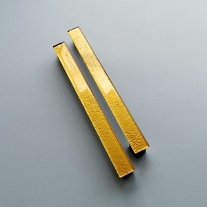 May include: Two gold-toned glass cabinet pulls, each with a rectangular shape and a smooth, polished finish.