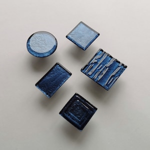 May include: Five blue glass tiles in different shapes and patterns. The tiles are arranged in a random pattern on a white background.