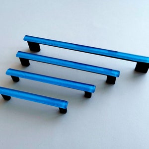 May include: Four blue glass cabinet pulls with black metal mounting brackets. The pulls are different lengths.