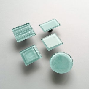 May include: Five different glass cabinet knobs in various shapes and sizes. The knobs are all a light blue colour and have a frosted finish.