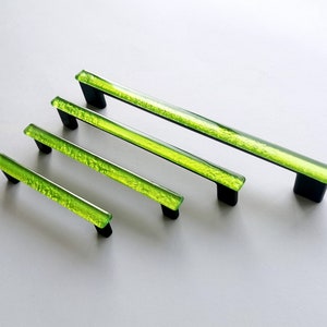 Op de afbeelding: Vier groene glazen kastgrepen met zwarte metalen bases. De grepen zijn in verschillende maten.